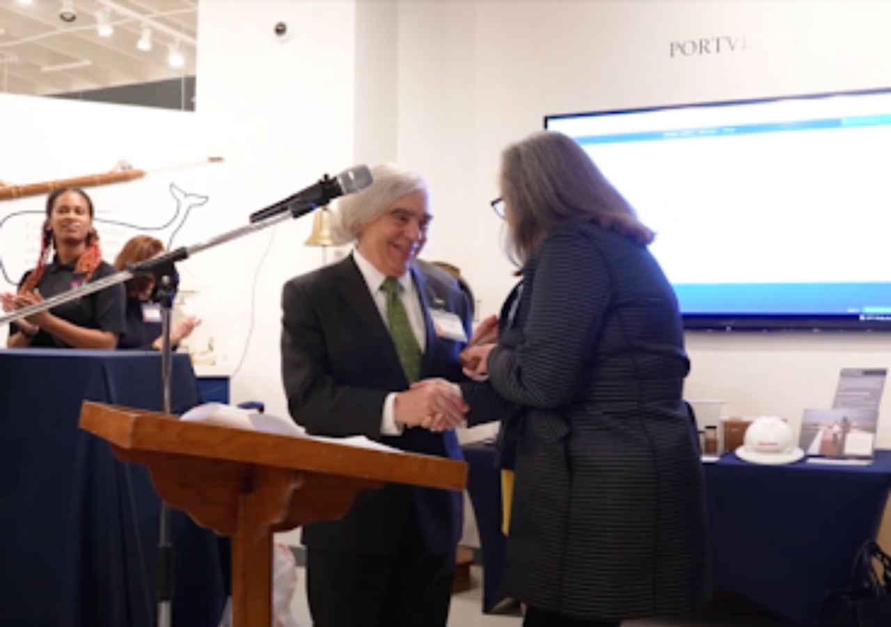 Photo of Ernest Moniz receiving the Award from Sarah Howell while at the podium.